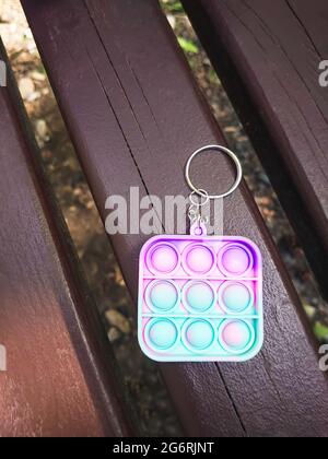 Porte-clés antistress en peluche accroché à un sac bleu, sur un banc de parc. Jouet en silicone pour soulager le stress. Mise au point sélective Banque D'Images