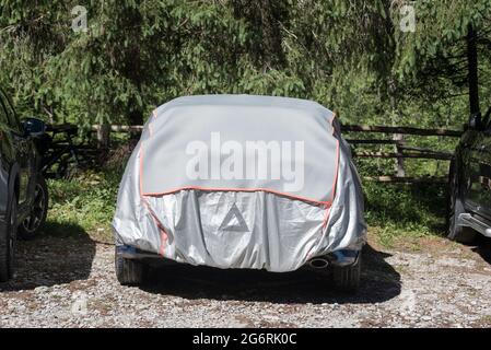 La housse de protection solaire grise et argentée. Voiture garée dans le parking de la forêt couvert d'un couvercle pour protéger contre le soleil et la poussière Banque D'Images