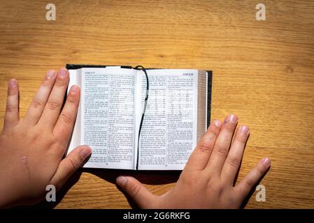 Les mains des enfants tiennent une bible penchée sur une table en bois. Petit livre Sainte Bible.Kid lecture de la sainte bible,closeup. Banque D'Images