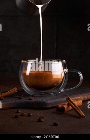 Café avec lait en verre sur fond sombre. Versez à la main de la crème de lait dans du café froid. Concept de boisson rafraîchissante savoureuse avec café. Copier l'espace Banque D'Images