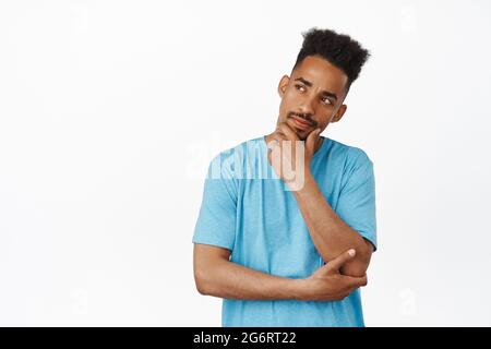 HMM, laissez-moi penser. Un homme afro-américain réfléchi touche son menton, furose et regarde de côté, réfléchit à la smth, prenant des décisions, pensant contre le blanc Banque D'Images