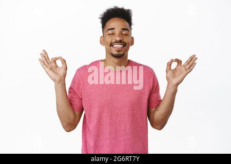 Paix et bonheur. Souriant soulagé afro-américain gars des yeux proches, tenant les mains dans om, Zen nirvana geste, Lotus yoga pose, méditant avec Banque D'Images