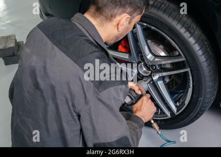 Mécanicien changeant la roue de voiture dans l'atelier de réparation automobile à l'aide d'une perceuse électrique pour desserrer les boulons. Concept de service ou de remplacement. Banque D'Images