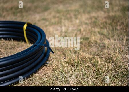 Bobine de tuyau d'irrigation de 1 pouce prête pour une nouvelle installation sur le dessus de l'herbe sèche brune et endommagée. Banque D'Images