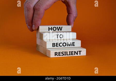 Comment devenir un symbole résilient. Concept de mots 'Comment devenir résilient' sur des blocs de bois sur un magnifique fond orange. Main d'homme d'affaires. Entreprise, Banque D'Images