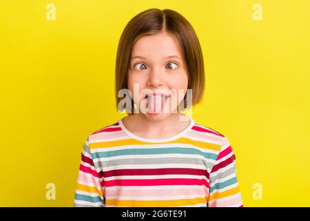 Photo portrait petite fille avec bob coiffure téméraire montrant la langue grimacing isolé couleur jaune vif fond Banque D'Images