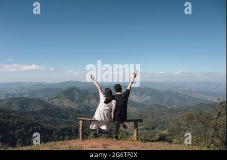 Jeune couple asiatique assis bras levés sur le sommet de la colline dans la campagne en vacances Banque D'Images