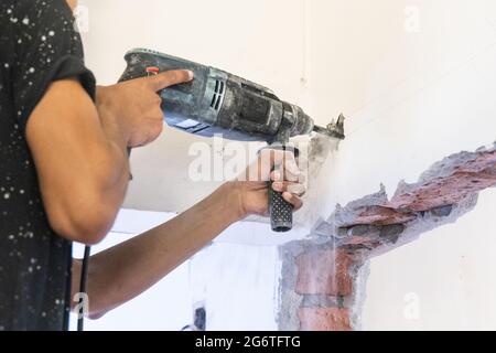 Les ouvriers forant sur le mur pour créer une cavité pour les câbles électriques dans la rénovation de la maison. Flou de mouvement intentionnel. Banque D'Images