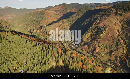 Le soleil des arbres d'automne sur les sommets de montagne. Personne aérienne nature paysage à la campagne. Route des cottages dans la vallée du mont. Vert, jaune sapin rural et forêt feuillue aux crêtes des Carpates, Ukraine, Europe Banque D'Images