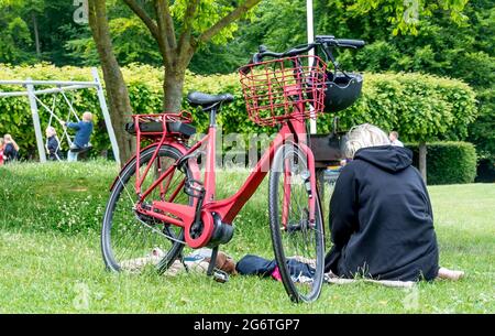 Aarhus, Danemark - 27 juin 2021 : les gens font un pique-nique et se promènent dans le parc commémoratif du château de Marselisborg, femme avec vélo rouge, livre de lecture Banque D'Images