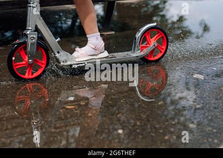 gros plan des jambes d'une fille dans des sandales d'été à travers une flaque sur un scooter, détente en famille et amusement Banque D'Images