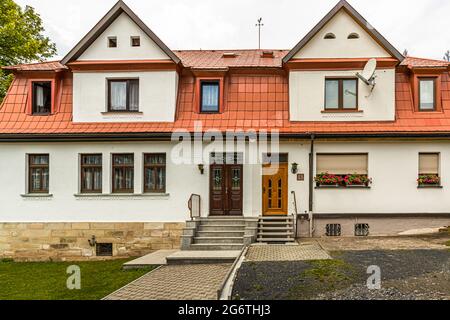 Une maison mitoyenne symétrique avec un toit en tuiles rouges et deux portes d'entrée conçues différemment se trouve à Steinach, en Thuringe, Allemagne, des géraniums fleurissent dans des jardinières sur la façade. Banque D'Images