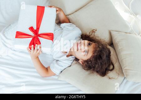 Une petite fille avec un cadeau se trouve dans le lit Banque D'Images