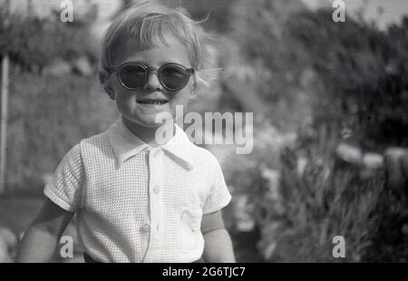 Années 1960, historique, à l'extérieur dans un jardin de cour, une petite fille portant une groovy paire de lunettes de soleil, Angleterre, Royaume-Uni. Banque D'Images