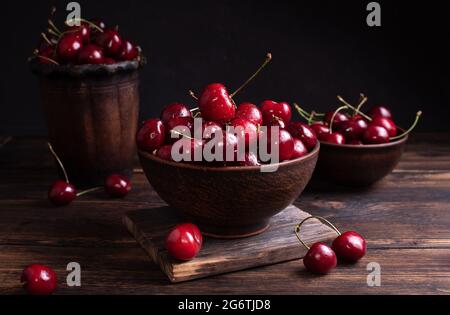 Cerises mûres dans des bols en argile sur une table en bois sombre, baies d'été utiles, style rustique. Banque D'Images