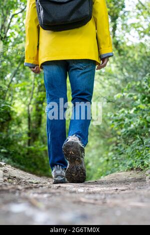 Vue arrière d'une personne portant un manteau jaune et un sac à dos marchant sur un sentier boueux, gros plan sur des chaussures. Banque D'Images