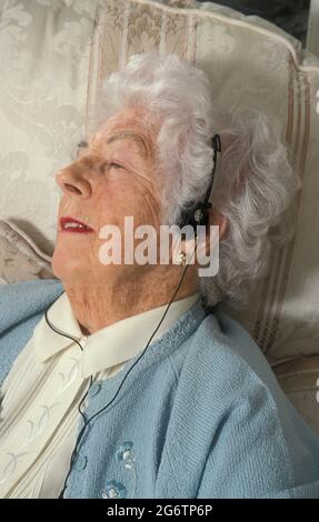 femme âgée se détendant dans un fauteuil, écoutant de la musique à l'aide d'un casque Banque D'Images