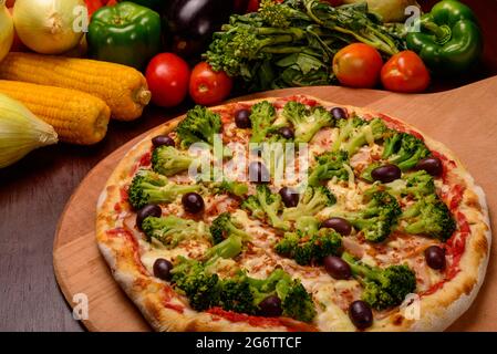 Pizza au brocoli avec olives noires sur bois et légumes en arrière-plan. Banque D'Images