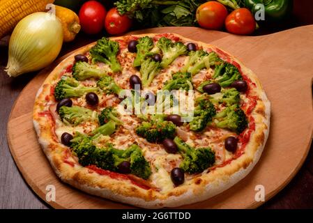 Pizza au brocoli avec olives noires sur bois et légumes en arrière-plan. Banque D'Images