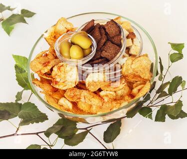 Été, composition alimentaire avec bière, encas solty : crackers de seigle, crackers de blé, chips de pomme de terre avec épices et olives vertes dans des bols en verre Banque D'Images