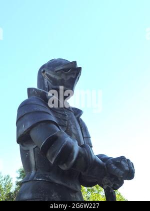 Un monument en pierre de chevalier médiéval en armure se dresse à l'extérieur contre un ciel bleu Banque D'Images