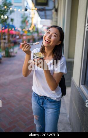 Bonne jeune femme asiatique manger un sandwich à la crème glacée dans un cadre urbain Banque D'Images