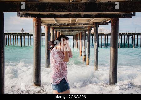 Turquie, Mer méditerranée. Une jeune femme s'est détournée de l'appareil photo, s'éloignant des vagues sous une jetée en bois. Banque D'Images