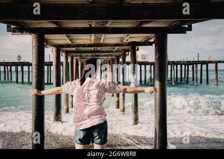 Turquie, Mer méditerranée. Une jeune femme s'est détournée de l'appareil photo, s'éloignant des vagues sous une jetée en bois. Banque D'Images