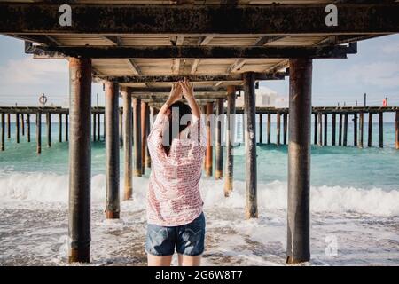 Turquie, Mer méditerranée. Une jeune femme s'est détournée de l'appareil photo, s'éloignant des vagues sous une jetée en bois. Banque D'Images