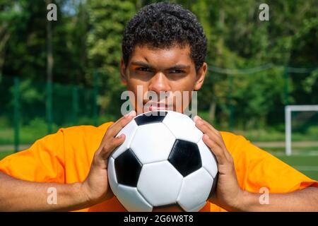 L'homme afro-américain tient le ballon de football de près tout en se tenant sur le terrain de sport Banque D'Images