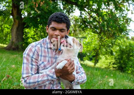 Afican homme américain tenant le chien Jack Russell dehors dans le parc en été Banque D'Images