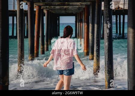 Turquie, Mer méditerranée. Une jeune femme s'est détournée de l'appareil photo, s'éloignant des vagues sous une jetée en bois. Banque D'Images