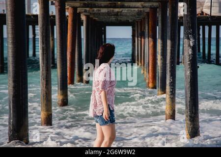 Turquie, Mer méditerranée. Une jeune femme s'est détournée de l'appareil photo, s'éloignant des vagues sous une jetée en bois. Banque D'Images
