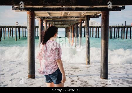 Turquie, Mer méditerranée. Une jeune femme s'est détournée de l'appareil photo, s'éloignant des vagues sous une jetée en bois. Banque D'Images