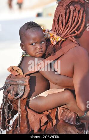 NAMIBIE. FEMME HIMBA PORTANT SON ENFANT SUR LE DOS. POUR LE PEUPLE HIMBAS, LES FEMMES ONT BEAUCOUP DE POUVOIRS COMME LA PROPRIÉTÉ DE CERTAINS DE LA VIE STOC Banque D'Images