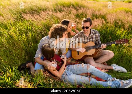 Amis assis ensemble dans l'herbe à jouer de la guitare et de refroidissement Banque D'Images