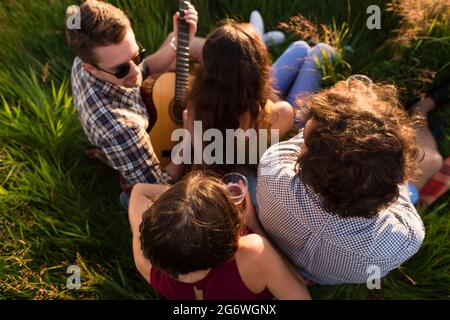 Amis assis ensemble dans l'herbe à jouer de la guitare et de refroidissement Banque D'Images