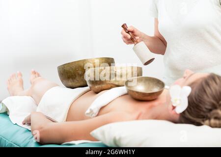 Gros plan d'une femme au spa avec des bols en cuivre recevant une thérapie sonore de cloche de chant Banque D'Images