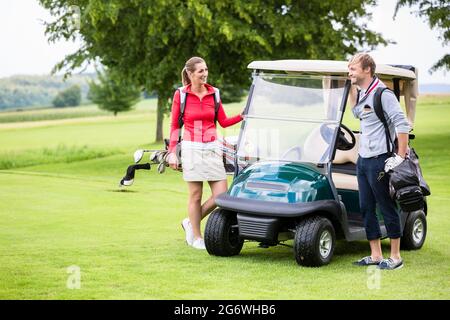 Heureux couple sportif debout près de la voiturette de golf regardant l'un l'autre Banque D'Images