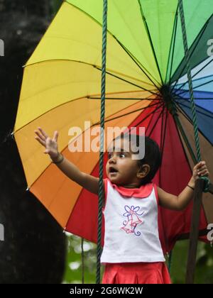 petite fille enfant essayant de prendre des gouttes de pluie tout en tenant un parapluie coloré Banque D'Images