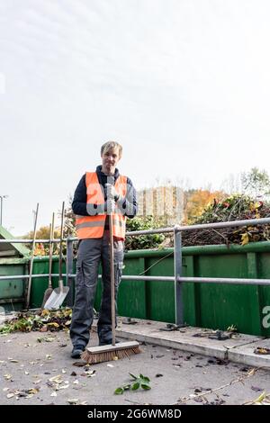 Homme balayant le sol du centre de recyclage après avoir placé le vert de déchets dans le conteneur Banque D'Images