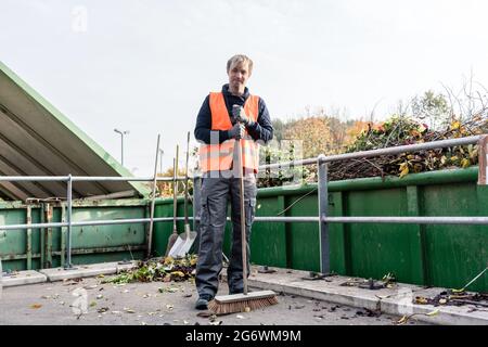 Homme balayant le sol du centre de recyclage après avoir placé le vert de déchets dans le conteneur Banque D'Images