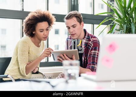 Deux jeunes employés regarder une vidéo sur tablet PC while sitting at desk dans le bureau Banque D'Images