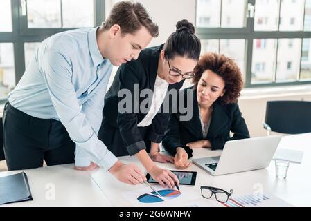 Jeune équipe de trois experts en affaires interprétant un graphique circulaire imprimé sur papier au bureau Banque D'Images