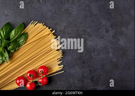 Spaghetti de pâtes italiennes aux feuilles de basilic et aux tomates sur fond texturé foncé, disposées dans les couleurs du drapeau italien. Vue de dessus. Copier l'espace Banque D'Images