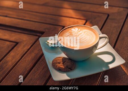 Latte dans une tasse de cappuccino à la table du café. Gros plan de la fleur de rosetta dessinant dans la mousse. Gros plan sur une tasse à café blanc cappuccino chaud en forme de cœur Banque D'Images