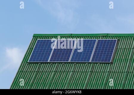 Quatre panneaux solaires sont installés sur la pente du toit de la maison. L'ardoise est rouge. Sur le fond d'un ciel bleu avec des nuages. Banque D'Images