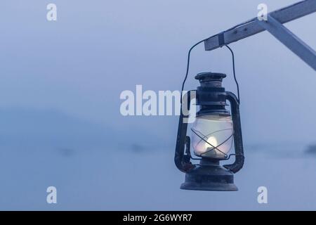 Une vieille lampe à kérosène en feu est suspendue sur un panneau en bois. Sur le fond de la mer et des nuages au crépuscule. Banque D'Images