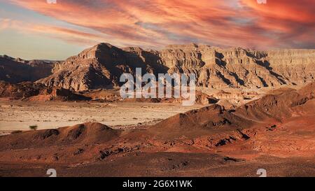 Paysage nocturne du désert d'Arava dans les couleurs rouges. Montagnes rouges, sable et nuages d'orange dans le désert du soir. Banque D'Images