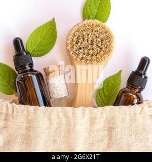 Sac réutilisable écologique en lin avec les différentes bouteilles et accessoires de salle de bains en bois naturel et en verre brun. Feuilles naturelles fraîches autour.C Banque D'Images